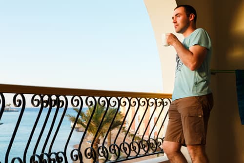 Man standing on balcony overlooking ocean portraying addict in luxury rehab facility