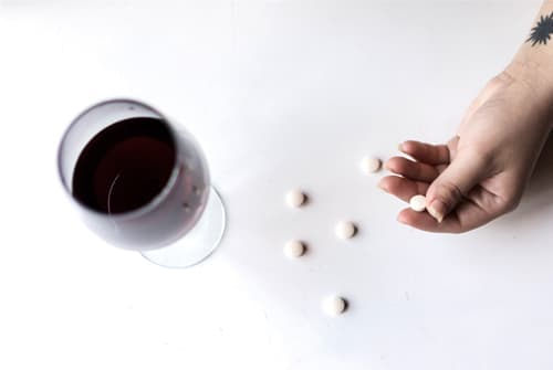 womans hand with pills and wine on table