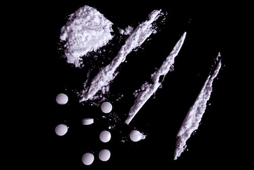 cocaine in lines and stimulant pills on black surface