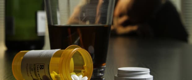 pill bottle and alcohol on table with sick man behind